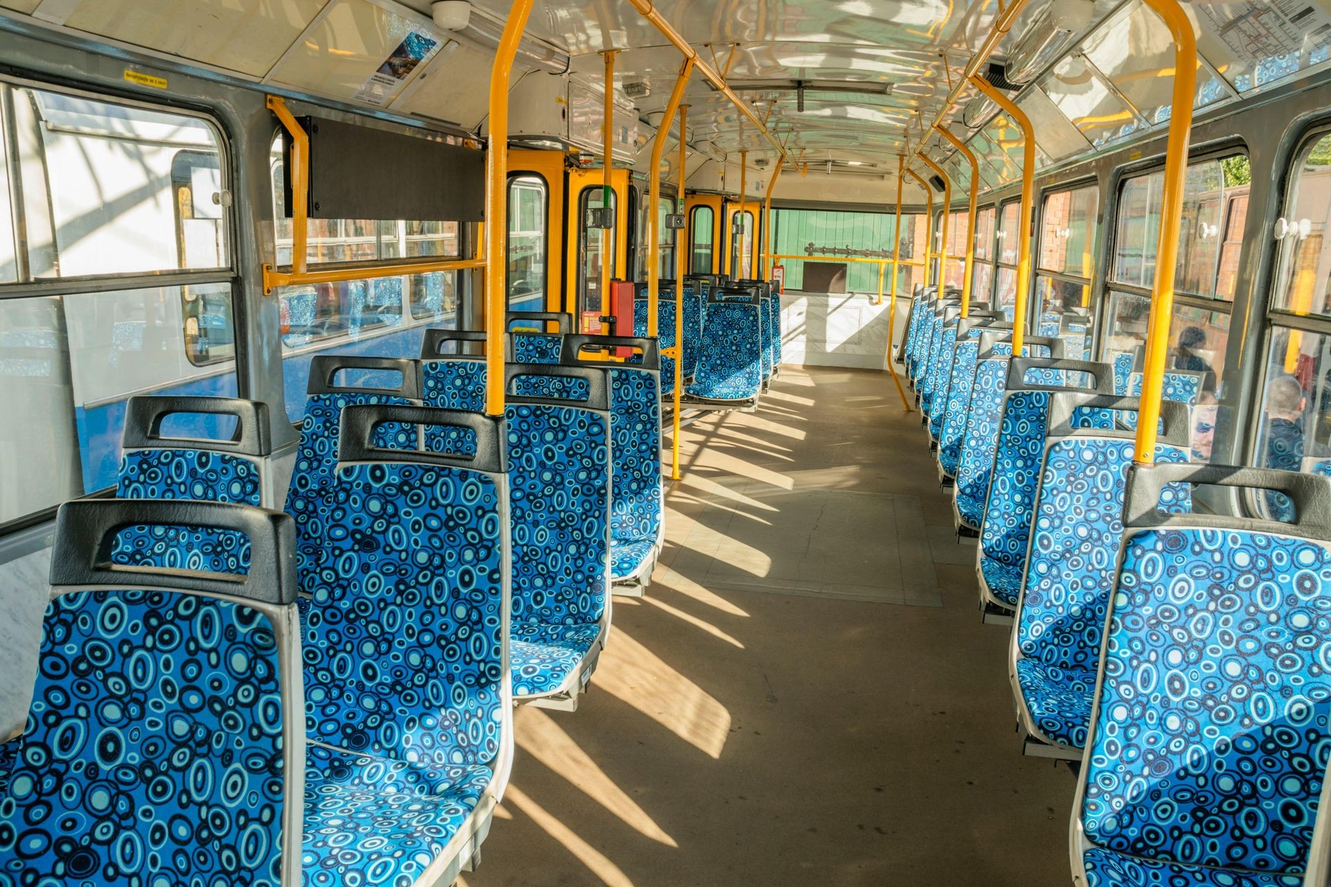 Interior of an empty city bus with patterned blue seats and yellow poles.